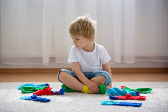 A young boy sitting on a rug and sorting colorful socks, a practical life activity using Montessori toys at home.