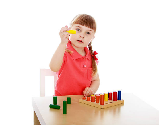 A young girl in a red polo shirt sorting colorful wooden cylinders on a board, focusing on Montessori toys for learning.