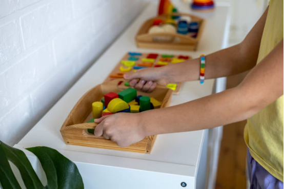 Child picking up a wooden tray of colorful building blocks, showcasing organized Montessori toys for early learning.