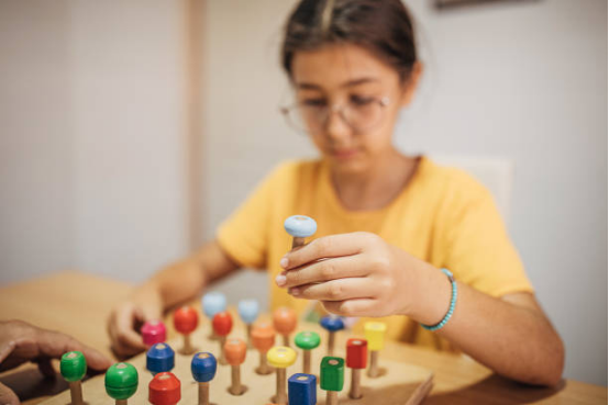 A bespectacled little girl is intently playing with Montessori toys.