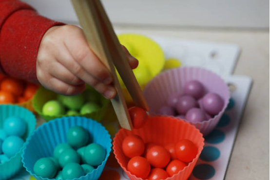 Close-up of a child using wooden tongs to sort colorful balls, a classic activity with Montessori toys.