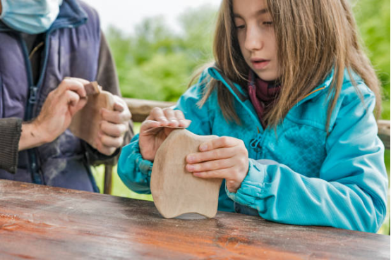 A young girl sanding a wooden shape outdoors, engaging with tactile Montessori toys for hands-on learning.