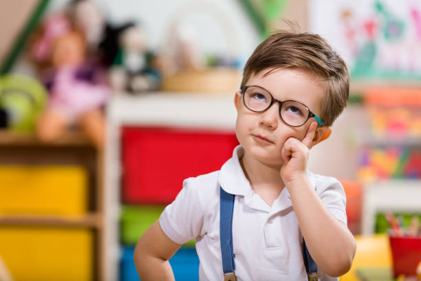 Thoughtful young boy in glasses, surrounded by Montessori toys in a classroom.