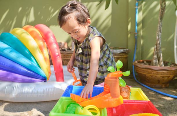 Toddler plays with water and colorful outdoor Montessori toys, encouraging sensory exploration.