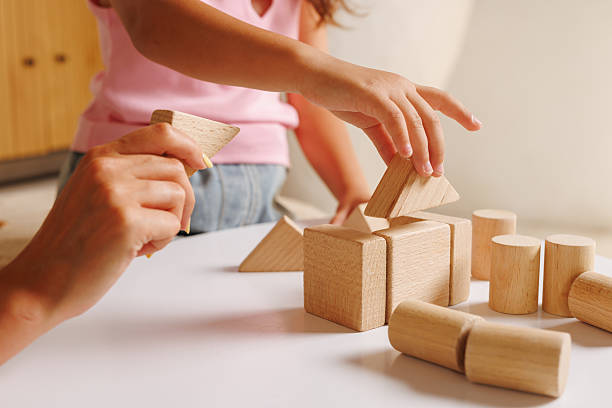 Child and adult hands stacking natural wooden blocks, engaging with Montessori toys.