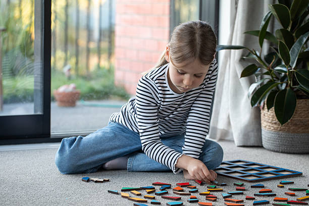 Girl playing with colorful wooden geometric Montessori toys on a living room carpet.