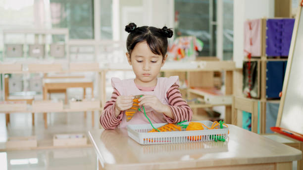 Focused girl learns fine motor skills with Montessori lacing carrot toys.