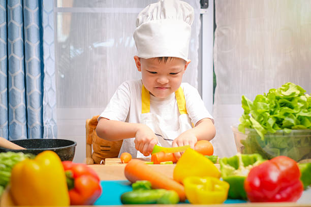 Young chef boy practices cutting vegetables using Montessori play kitchen toys.