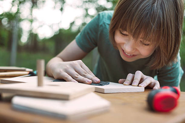 Smiling child sanding wooden pieces, engaging in hands-on creation of Montessori toys.