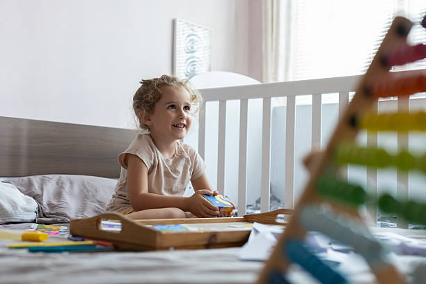 Smiling child on bed, joyfully engaging with colorful wooden abacus Montessori toys.
