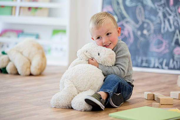 Happy child hugging a plush toy, with wooden Montessori toys blocks nearby on the floor.